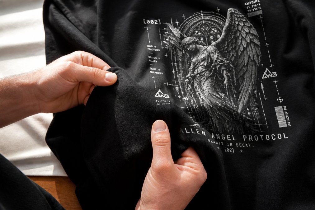 Close-up of hands examining the dense weave and texture of a heavyweight cotton graphic tee, showing the fabric weight and print clarity against natural window lighting