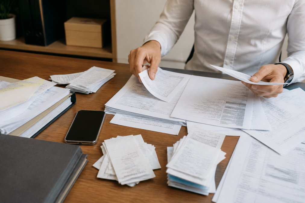 Hands organizing tax documents and receipts on desk, smartphone displaying document scanning app nearby, professional workspace lighting