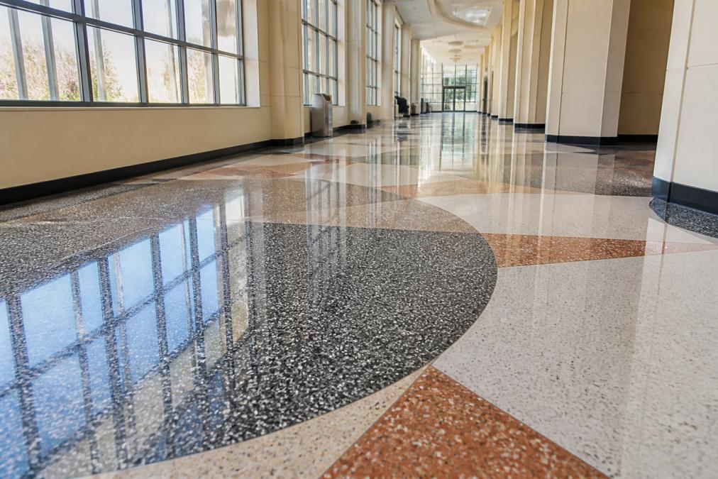 Close-up of polished terrazzo flooring with custom aggregate inlays and geometric patterns in a modern institutional hallway with natural light reflecting off the finished surface