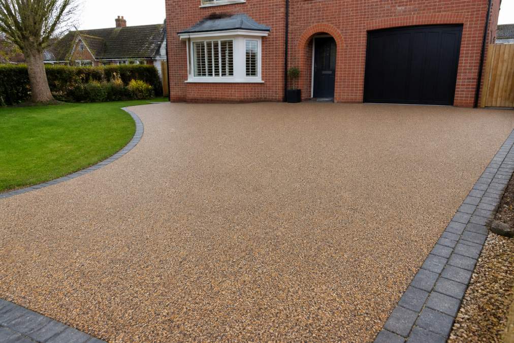 A newly finished resin bound driveway in front of a red brick Norfolk home, with a smooth, evenly textured surface and a neat block paving border along the edges