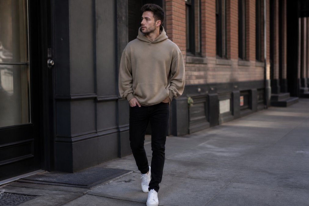 Person wearing a drop shoulder hoodie styled with fitted black jeans and minimal accessories, demonstrating balanced proportions with the relaxed upper body contrasted against tapered lower body, photographed in natural daylight