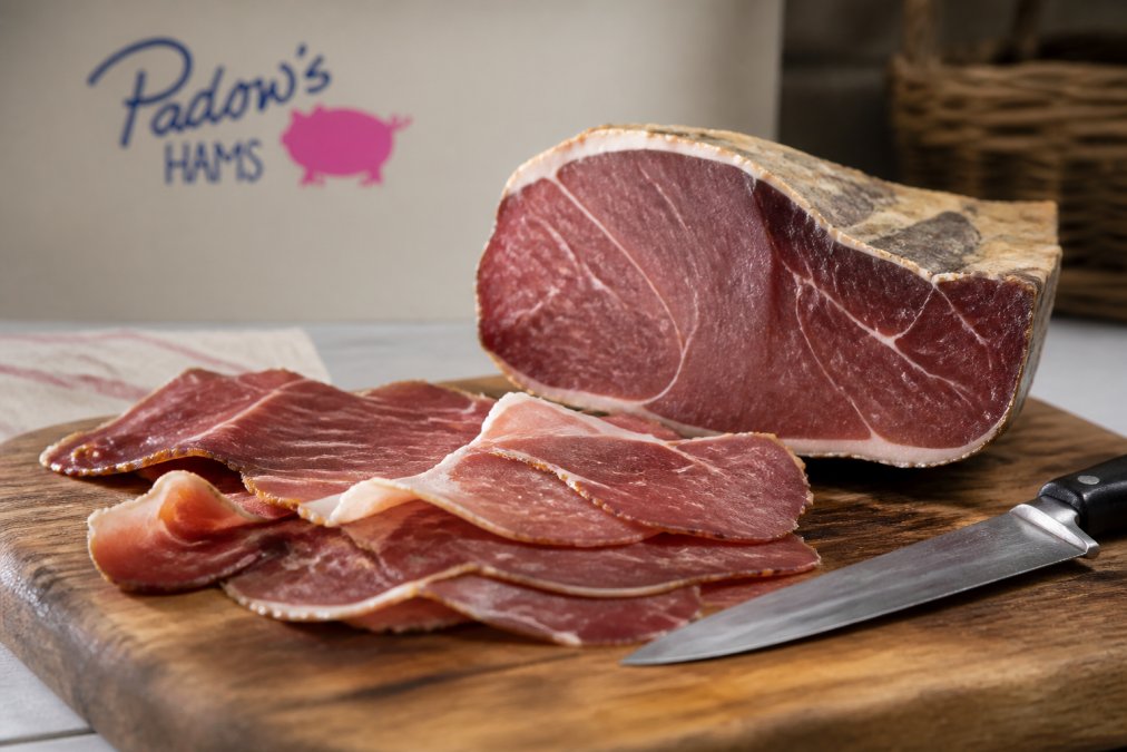 Sliced dry-cured Virginia ham on a wooden cutting board with a sharp knife, showing the deep mahogany color and dense texture of the meat, natural kitchen lighting