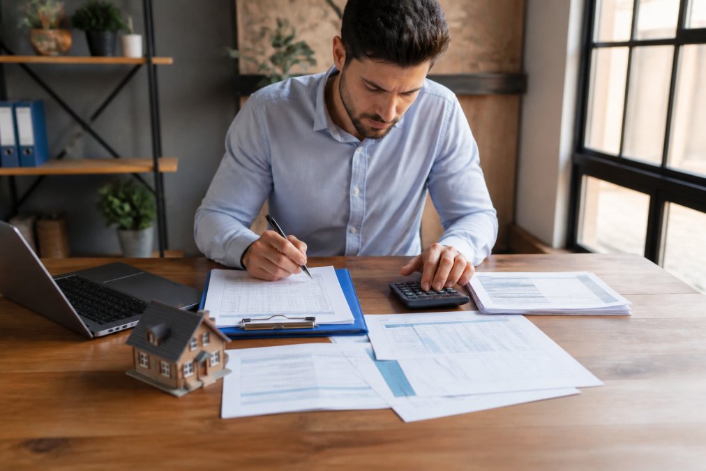 Real estate investor reviewing property financial statements and rental income documentation at a desk with laptop, calculator, and lease agreements in natural office lighting