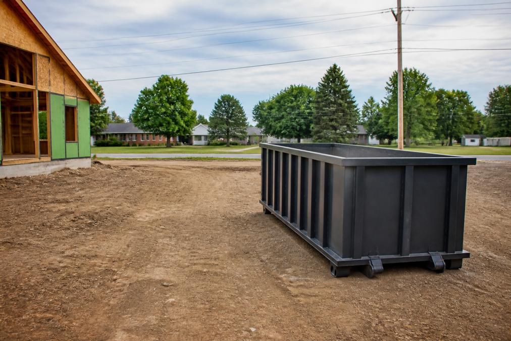 A roll-off dumpster positioned on a level construction site with clear access for delivery trucks, showing proper placement away from utilities, overhead power lines, and nearby structures