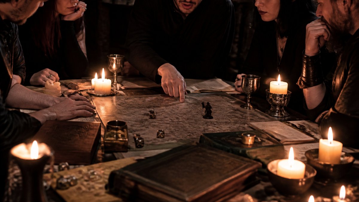 A moody tabletop scene with adults gathered around a candlelit table, weathered rulebooks and dice scattered across a dark fantasy map, one player pointing at a location while others lean in