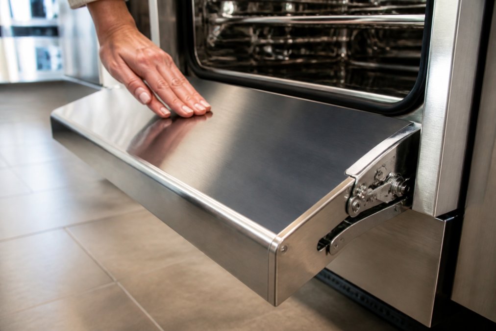 Hand running over the brushed stainless steel door of one of our premium kitchen appliances in a bright showroom