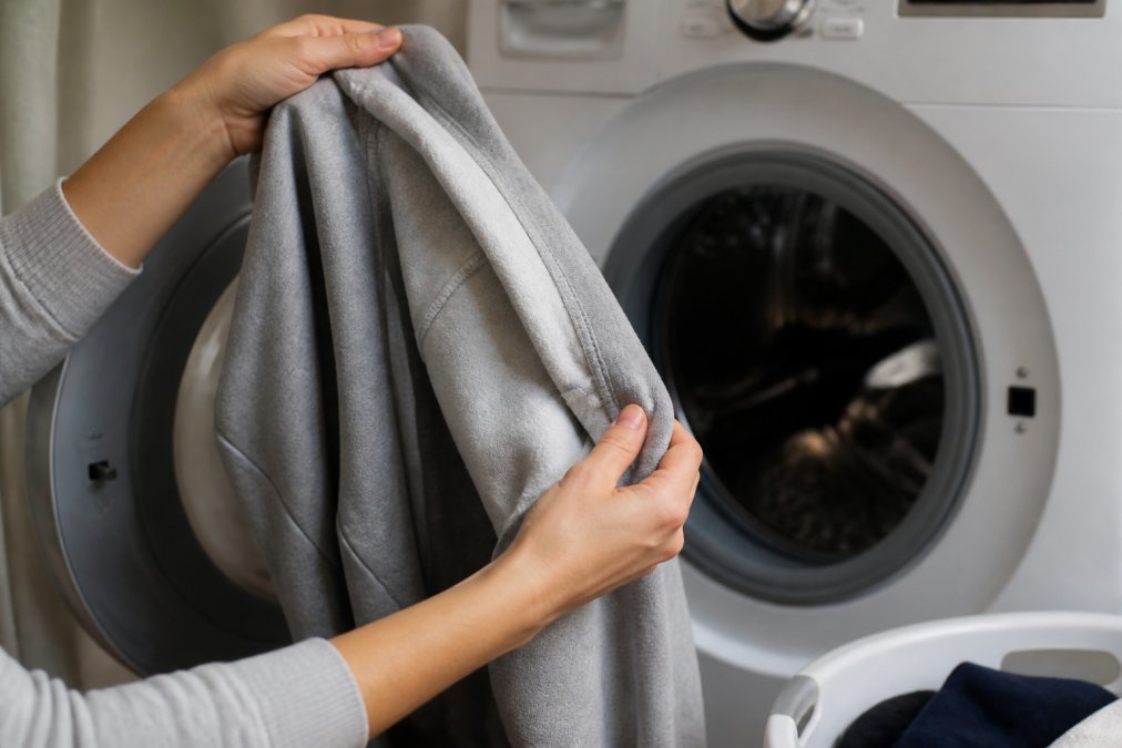 Close-up of hands turning a sweatshirt inside-out before placing it into a washing machine, showing proper care technique