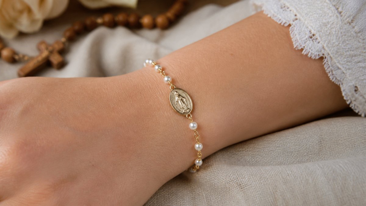 Close-up of a woman's wrist wearing a delicate gold-tone Miraculous Medal bracelet with pearl accents, resting on a soft neutral fabric, natural light
