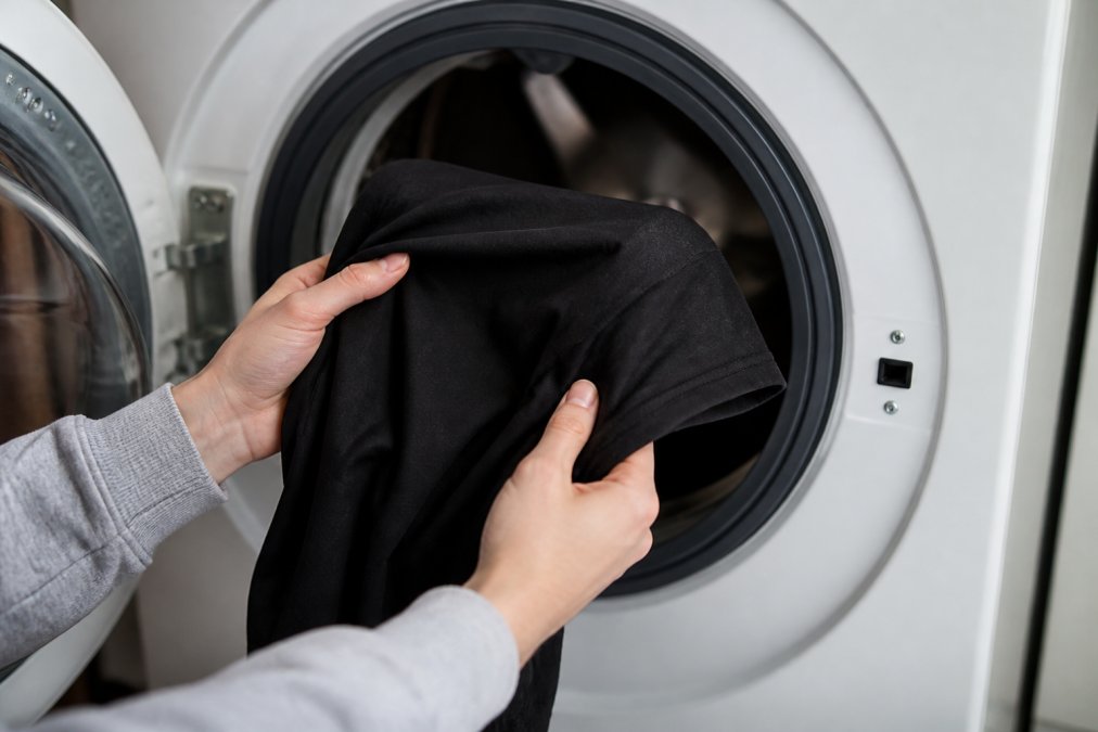 Hands carefully turning a durable funny graphic tee inside out before placing it in a washing machine, showing proper care technique with soft natural lighting