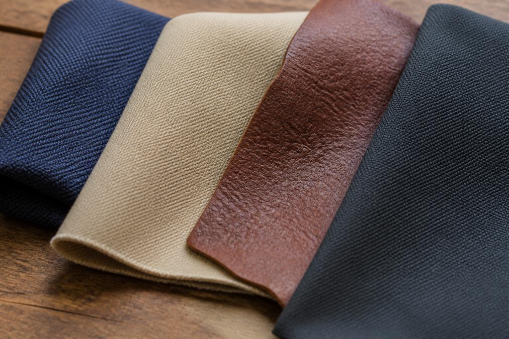 Close-up of different hat materials displayed on a wooden surface showing polyester weave, cotton twill texture, leather grain, and synthetic fiber construction under natural lighting