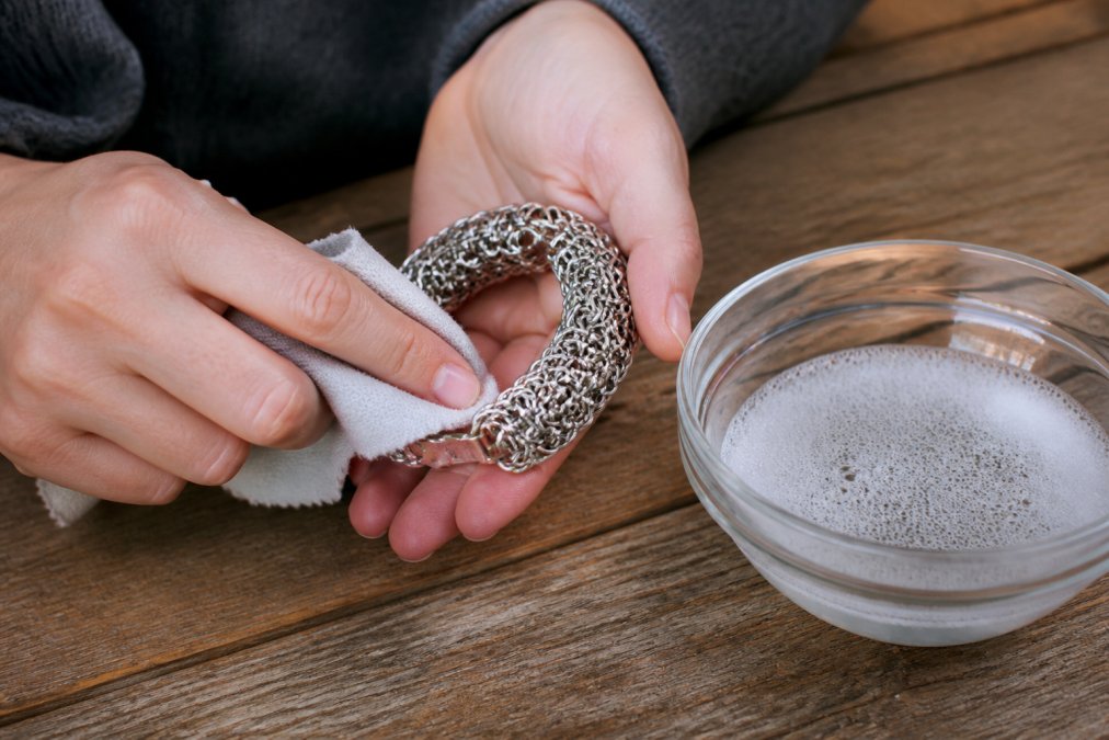 Step-by-step guide for cleaning your durable jewellery using a soft cloth and mild soapy water on a wooden surface.