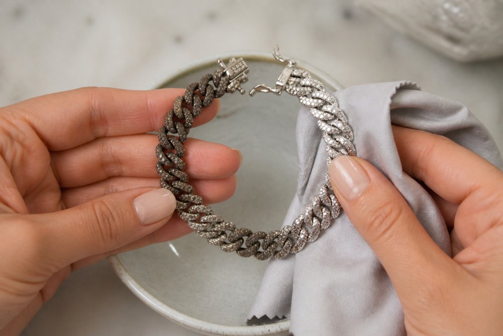 Hands gently polishing a tarnished silver bracelet with a soft microfiber cloth over a small ceramic bowl, showing the visible contrast between the dull tarnished area and the brightening polished section as the cloth removes oxidation