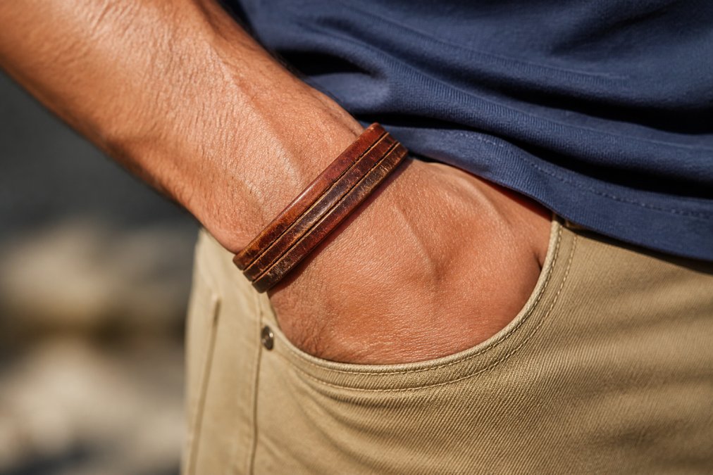 Close-up of a man's wrist wearing a well-worn leather bracelet showing visible patina and rich color variation, with natural sunlight highlighting the grain texture and aged character