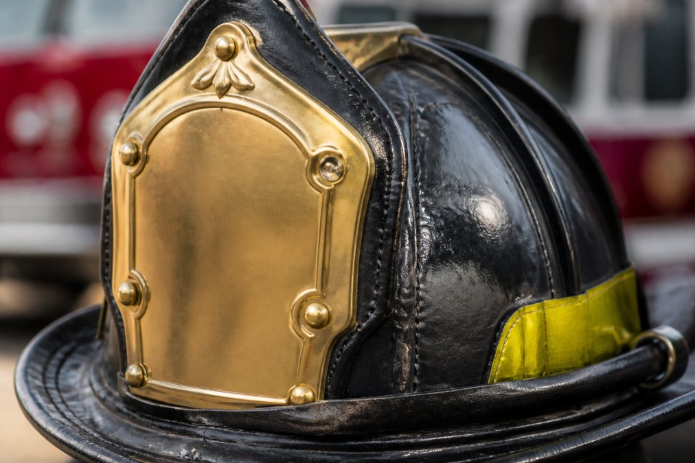 Close-up of a firefighter's leather helmet displaying a polished brass front holder in detail, showing the craftsmanship and metalwork and intricate riveting