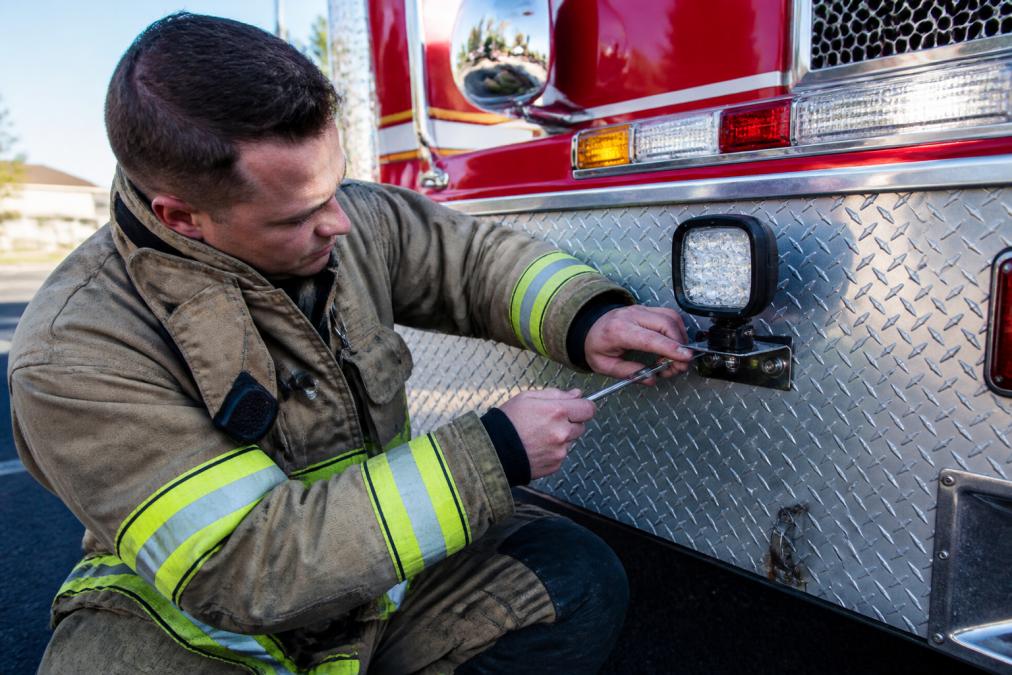 Firefighter inspecting the mounting bracket of durable LED lighting for fire trucks on a diamond-plate truck body