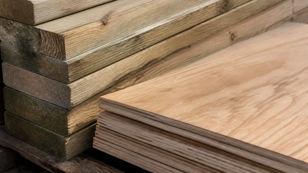 Close-up of stacked pressure-treated cedar lumber and exterior-grade plywood showing natural wood grain texture and weathered finish in natural daylight