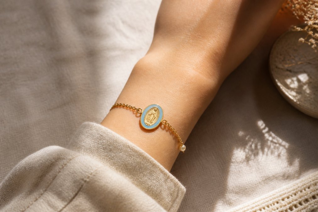 Delicate gold-plated medal bracelet with soft enamel accents resting on a linen tablecloth in natural light