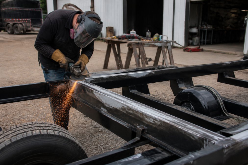 Worker grinding the metal frame of heavy duty trailers to prepare for painting