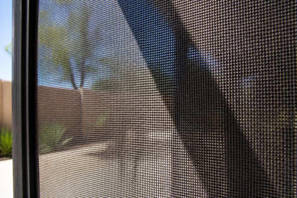 Close-up of solar screen fabric showing mesh texture and protective coating with bright sunlight creating distinct shadows through the material, highlighting the weave pattern and UV-resistant surface