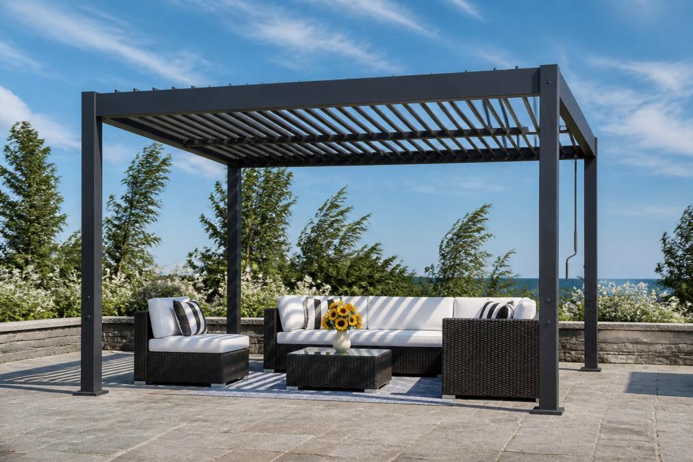 A sleek black powder-coated aluminum louvered pergola installed on a stone patio with adjustable louvers partially open, photographed against a bright blue sky with visible wind movement in surrounding trees