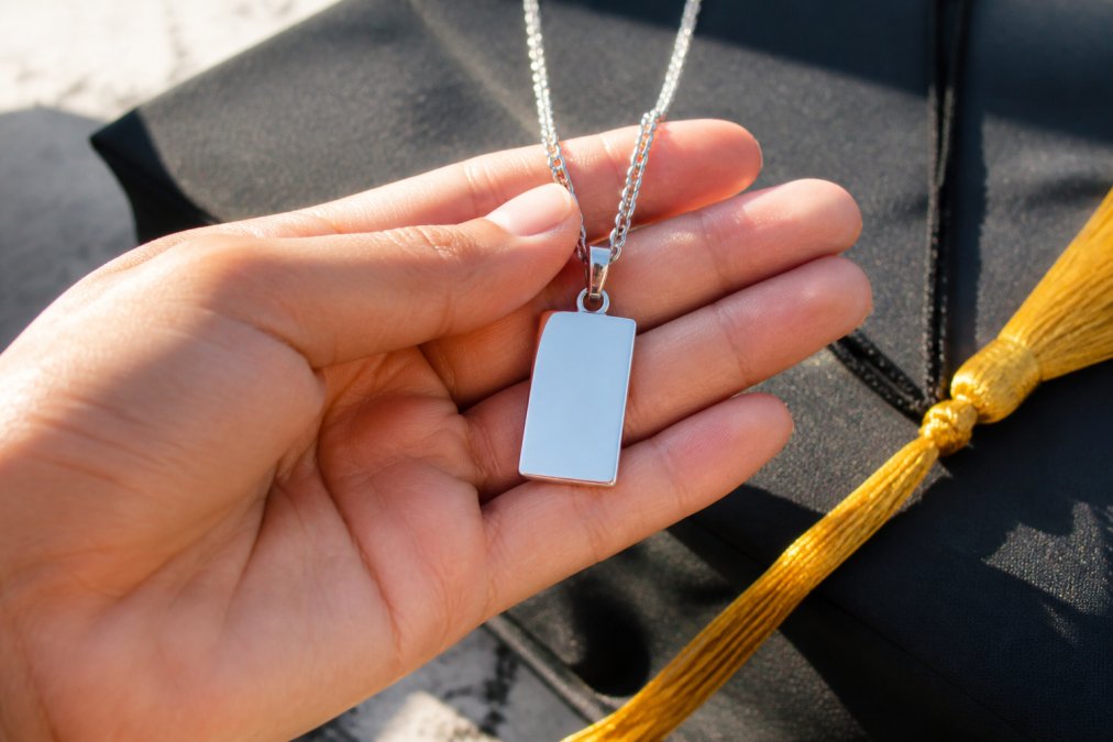 A hand holding a gleaming stainless steel personalized necklace with an engraved pendant, showing the lustrous finish and clarity of the metal under natural sunlight