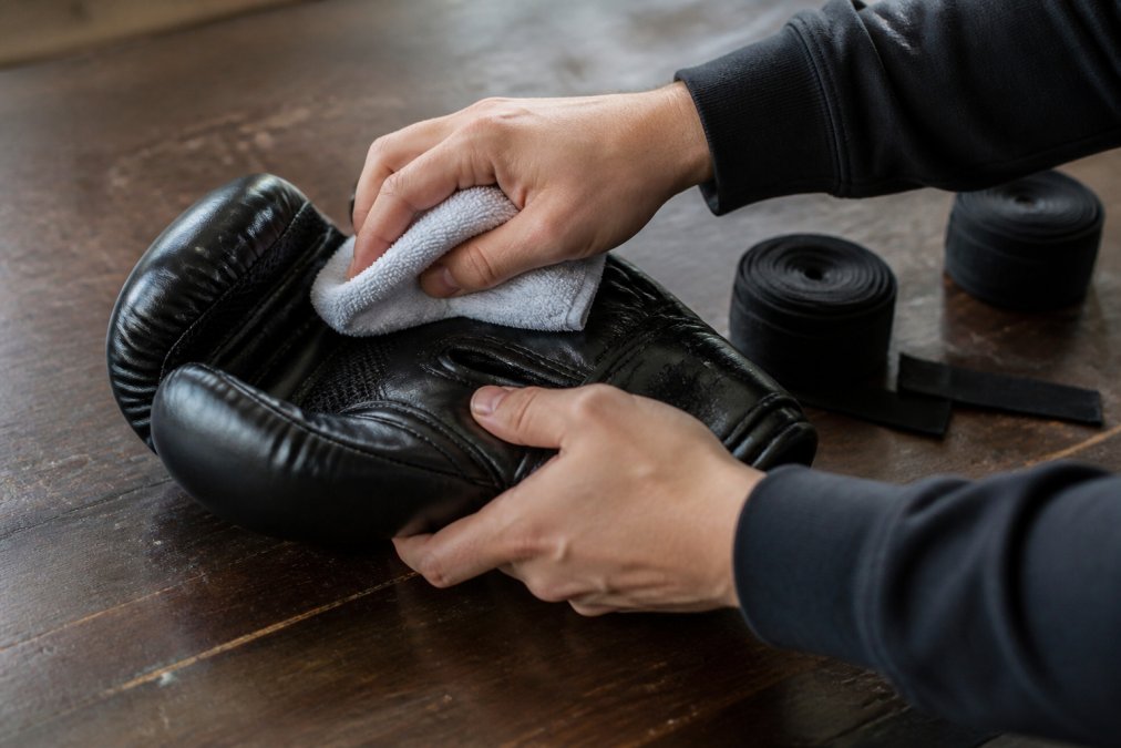 Close-up of hands cleaning and inspecting protective gear like gloves and hand wraps after a training session, showing proper maintenance technique
