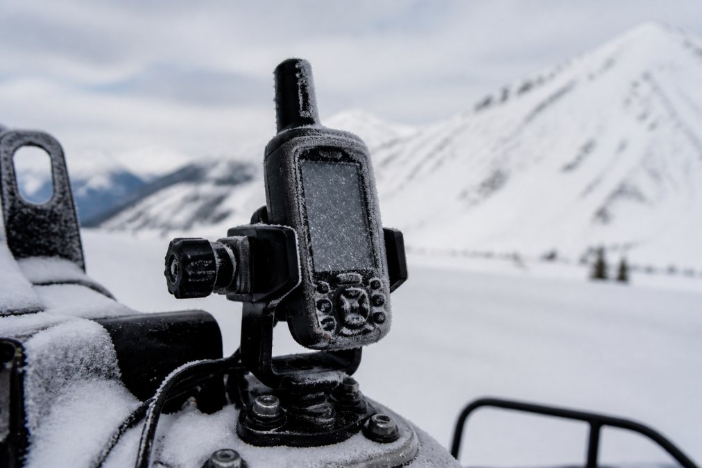 Outdoor scene of a handheld GPS device mounted on field equipment in a snowy, cold environment with visible frost on the device and surroundings, demonstrating real-world cold-weather deployment