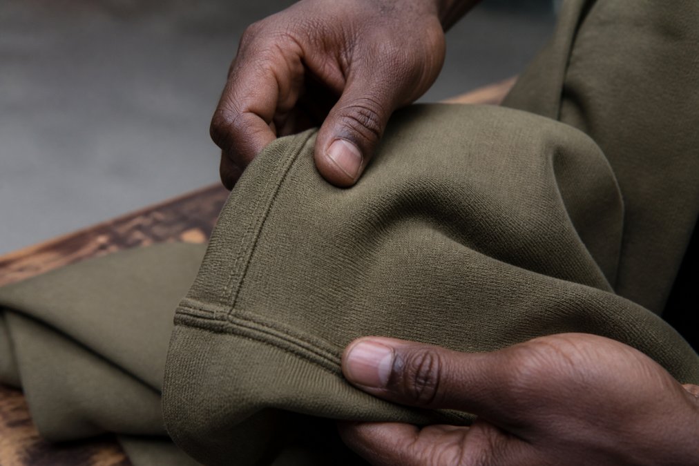 Close-up of premium durable cotton fabric showing dense weave, tight stitching detail, and hands touching the material to demonstrate weight and quality