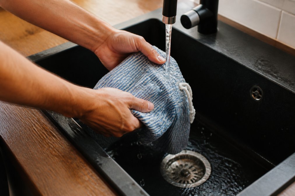 Close-up of hands carefully rinsing seersucker swim shorts under cool running water, demonstrating proper care technique to preserve fabric weave and seam integrity