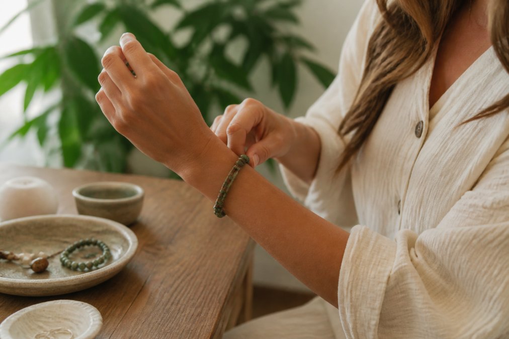 Vrouw die voorzichtig een handgemaakte armband om haar pols doet, met aandacht en intentie, in een rustige, natuurlijke omgeving