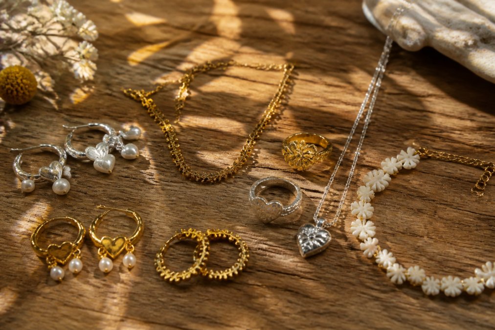 Close-up van verschillende duurzame sieraden in zilver en goud, uitgestald op een natuurlijk houten oppervlak met zacht daglicht dat de details van de ambachtelijke afwerking benadrukt