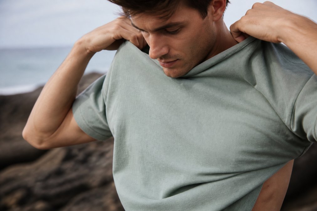 Close-up van iemand die voorzichtig een duurzaam katoen streetwear shirt aantrekt, met zichtbare textuurdetails en natuurlijke verlichting