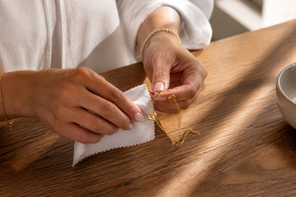 Iemand die voorzichtig een zilveren armband schoonmaakt met een zachte microvezel doek op een houten tafel, met natuurlijk daglicht dat het detail benadrukt
