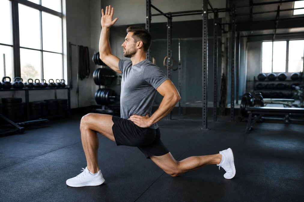 Professional demonstrating dynamic hip flexor stretching technique in modern gym setting with proper form and alignment