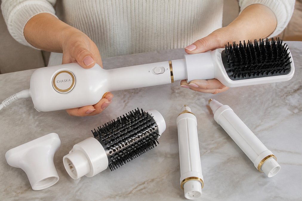 Close-up of hands demonstrating different styling attachments on a multi-function hair tool, showing the switch between drying, straightening, and curling modes with professional precision