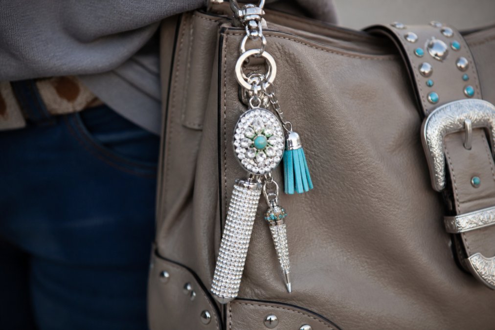 Close-up of a designer-inspired rhinestone safety keychain with Western-inspired accents attached to a fashionable leather handbag, showing how personal safety gear integrates seamlessly into daily style
