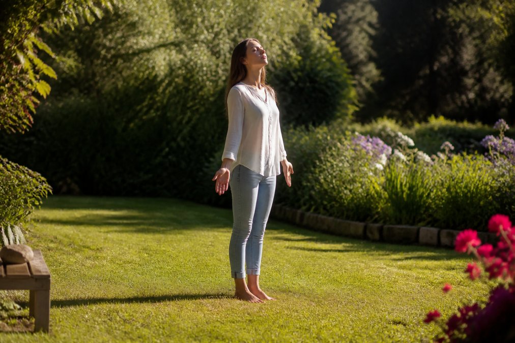 Earthing and Grounding for Spiritual Wellbeing 1 Woman standing barefoot on grass in natural sunlight, eyes closed, arms relaxed at sides, peaceful expression, garden or park setting