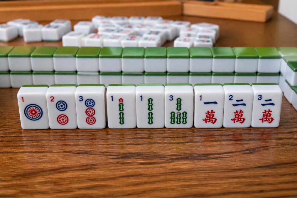 Close-up of mahjong tiles arranged on a table showing a consecutive run hand pattern with numbered suits clearly visible, tiles displaying 1-2-3 sequences in multiple colors under soft natural lighting