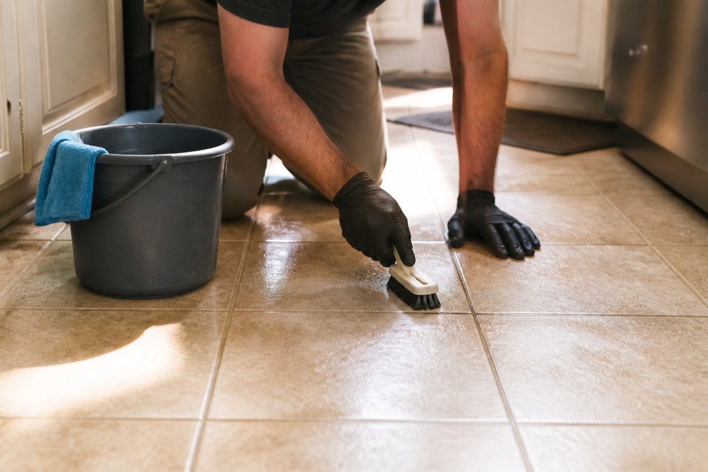 Hands scrubbing a kitchen floor to prepare for selling home quickly by cleaning tile and bright grout lines