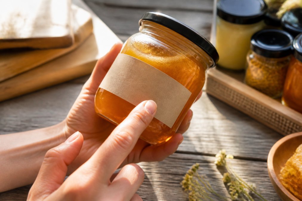 Nahaufnahme einer Hand, die ein Honig-Glas hält und das Etikett mit Herkunftsangabe und Inhaltsstoffen prüft, natürliches Licht von oben