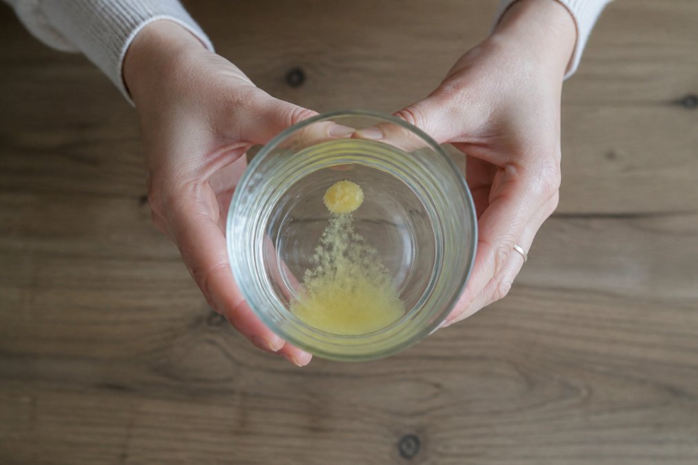 Hände beim Wasserlöslichkeitstest, um echten Naturhonig erkennen zu können, während ein Honigtropfen langsam im Glas nach