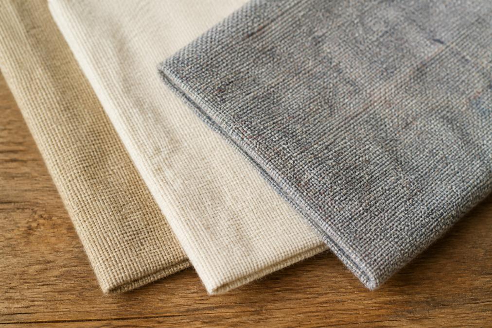 Close-up of fabric swatches showing hemp, linen, and recycled fiber textures with visible weave patterns laid flat on natural wood surface with soft window lighting