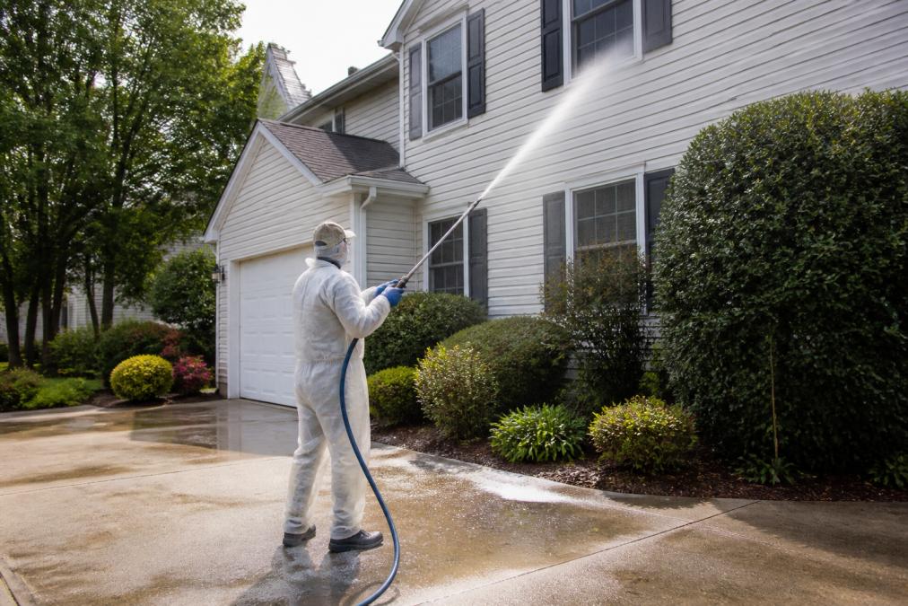 Technician using a soft wash system for eco friendly exterior home cleaning on a two-story vinyl siding house.