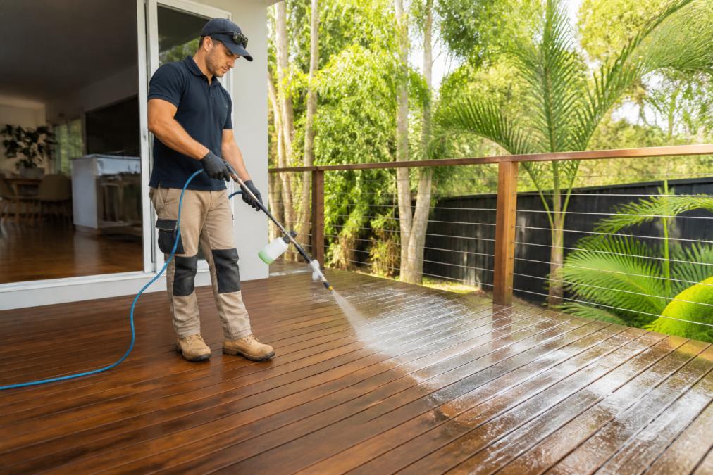 Technician using eco-friendly pressure cleaning on a timber deck with a low-pressure soft washing sprayer