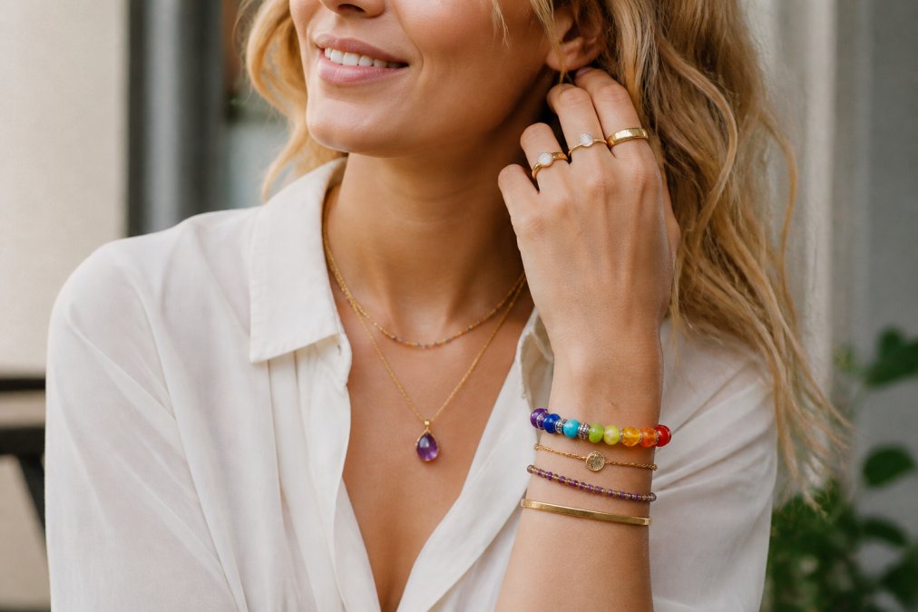 Vrouw draagt meerdere edelsteen armbanden samen met andere sieraden, kettingen en ringen, in een natuurlijke dagelijkse setting, waarbij de combinatie gebalanceerd en stijlvol oogt