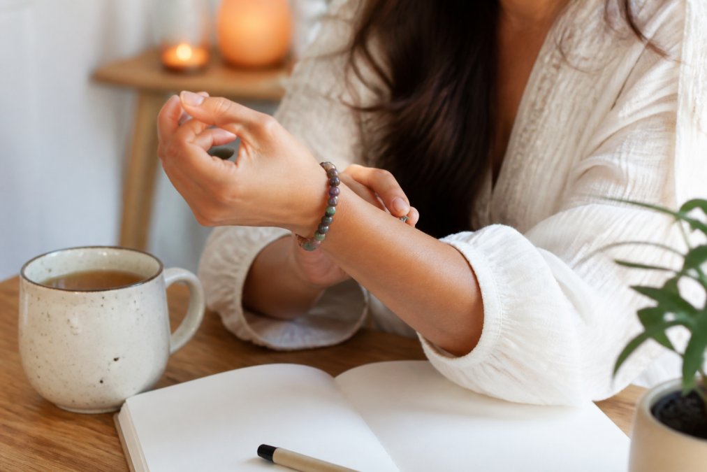 Vrouw doet een kleurrijke edelsteen armband om aan een sfeervol verlichte tafel met thee en een notitieboekje.