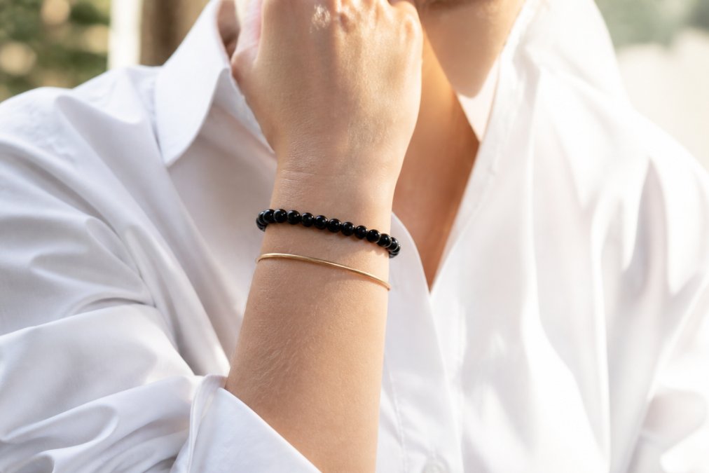 Zwarte onyx kralenarmband gecombineerd met een gouden armband als stijlvolle edelsteen sieraden bij een wit overhemd.