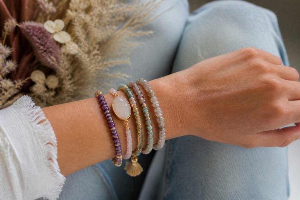 Nahaufnahme eines weiblichen Handgelenks mit mehreren elegant gestapelten Edelstein-Armbändern in verschiedenen Farben und Materialien, die einen zeitlosen Look zeigen