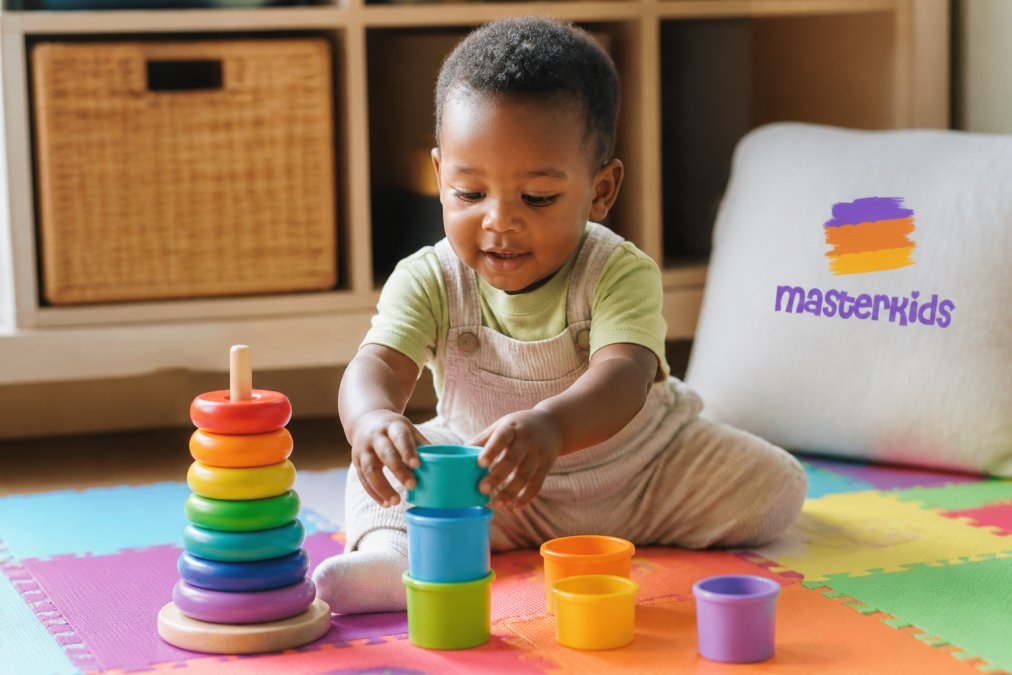 A 2-year-old child playing with colourful wooden stacking rings and nesting cups on a bright play mat, hands actively engaged in sorting and stacking different sized pieces