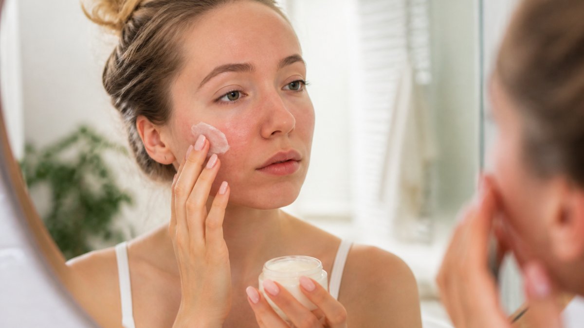 Close-up of a woman with sensitive skin gently applying a soothing cream to her face in a bright bathroom, soft natural light, calm atmosphere